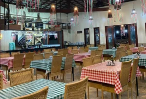 Ambiente Acolhedor da Nossa Pizzaria em Luís Correia - Bellissima Italia Salão amplo e arejado da Pizzaria em Luís Correia Bellíssima Itália, com mesas de madeira cobertas por toalhas xadrez e teto alto com vigas de madeira aparente.