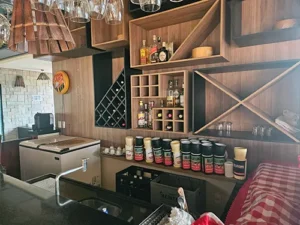 Bellissima Italia: Drinks, Vinhos e Cervejas em Nosso Bar Aconchegante Área do bar bem abastecido da Pizzaria e Restaurante Bellissima Italia em Luís Correia, com prateleiras de madeira, diversas garrafas de bebidas, taças de vinho penduradas e balcão.
