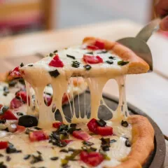 Fatia de pizza sendo levantada com uma espátula, mostrando o queijo muçarela derretido e esticando, na Pizzaria Bellissima Italia em Luís Correia.